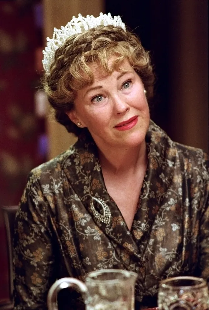 Catherine O'Hara wearing a tiara, silk robe, and pink lipstick, looking off-camera.