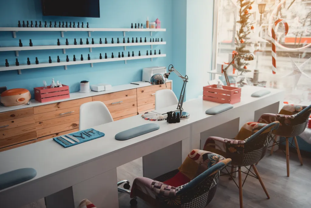 Modern beauty salon with nail appliances on a long desk, colorful chairs, and shelves of nail polish.