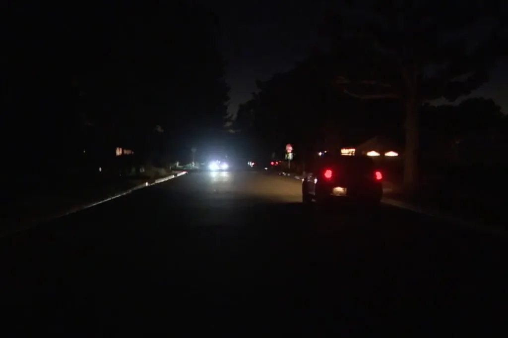 A dark street at night, with a car's taillights visible on the right and another car's headlights in the distance.
