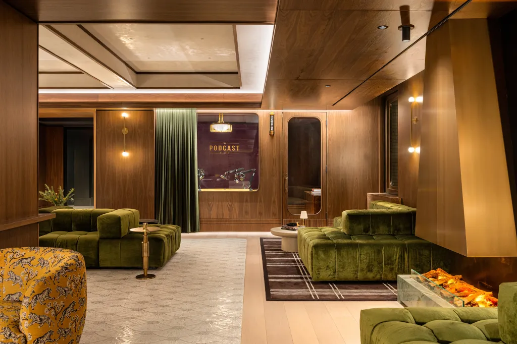 An opulent Grand Central Podcast Gallery lounge area with plush green velvet couches and a glass-enclosed fireplace.