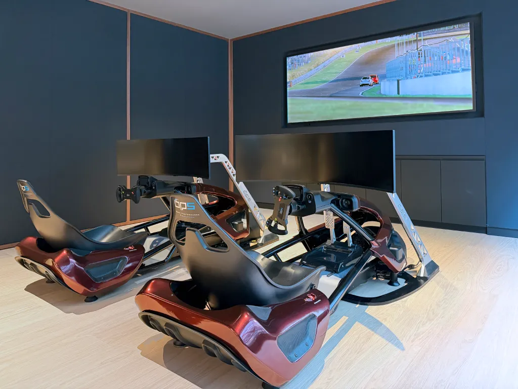 Two racing simulators with large screens and bucket seats in a room with dark blue walls and light wood flooring.