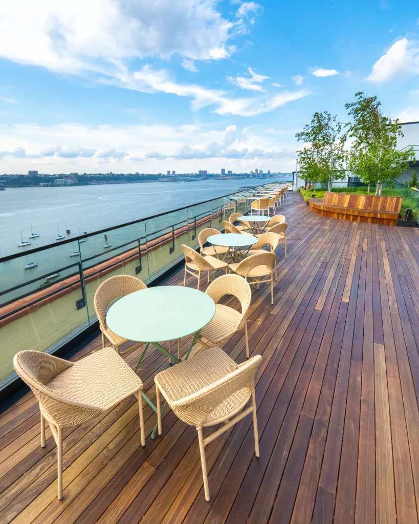 Rooftop deck with tables and chairs overlooking the Hudson River.