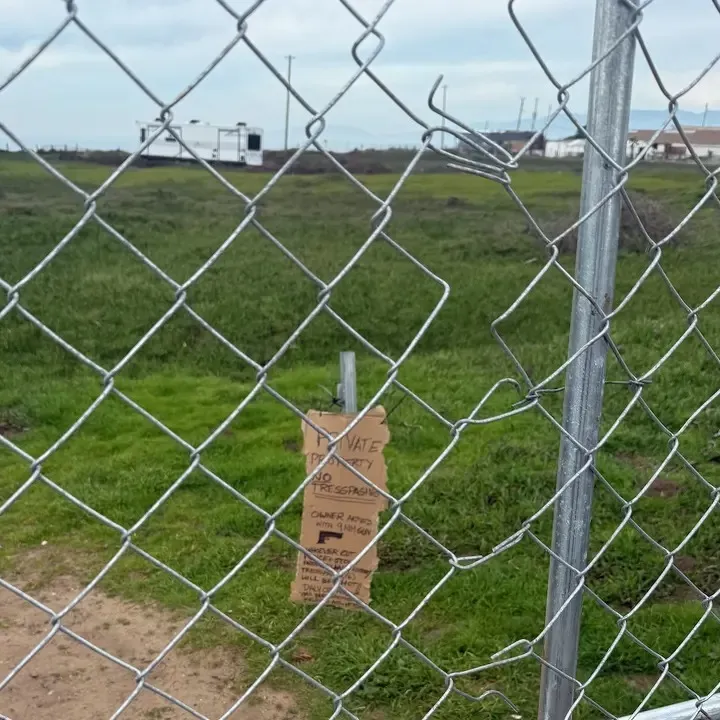 A chain-link fence blocks a dirt path with a sign warning 