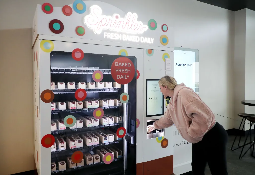 A woman buying a cupcake from a Sprinkles vending machine.