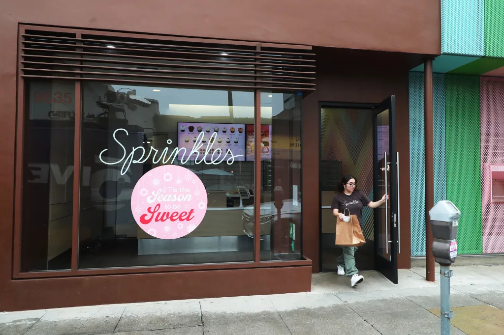 A woman exits the Sprinkles cupcake store in Beverly Hills with a brown paper bag, reflecting the company's impending closure.
