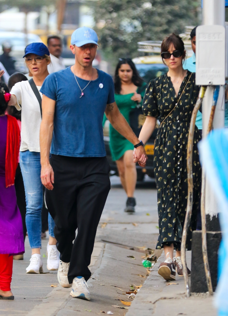 Chris Martin and Dakota Johnson hold hands while walking on a crowded street in Mumbai.