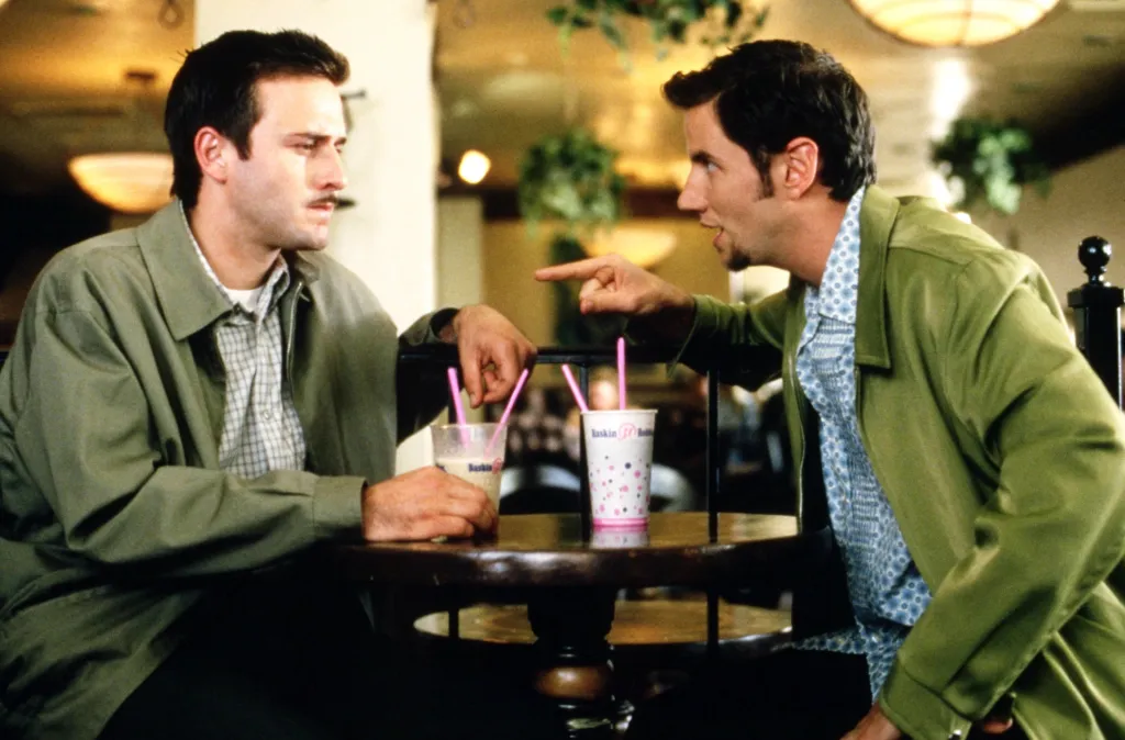 David Arquette and Jamie Kennedy sitting at a table with drinks in Scream 2.
