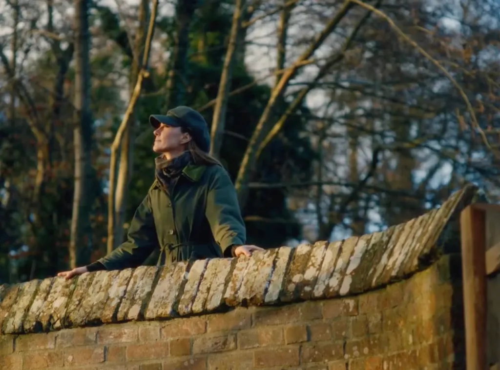 Kate Middleton looking up while leaning on a brick wall.