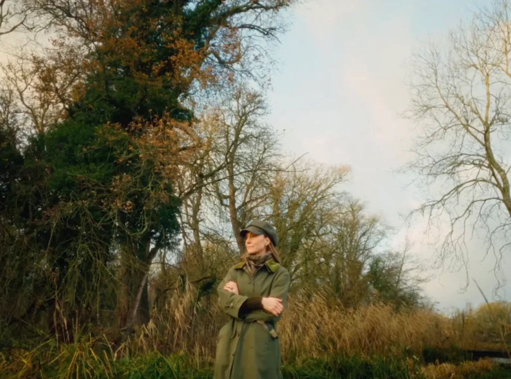 Kate Middleton stands outdoors, arms crossed, wearing a green coat and cap.