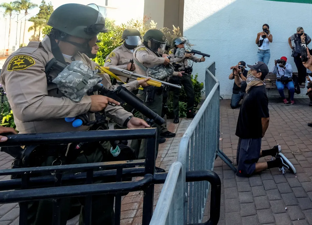 A demonstrator kneels as Los Angeles County sheriff's deputies aim weapons at a protest in Compton.
