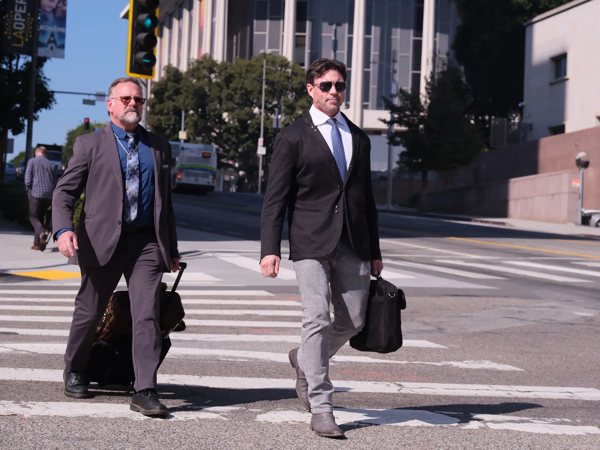 Aaron Phypers (right) and a man in a gray suit cross a street.