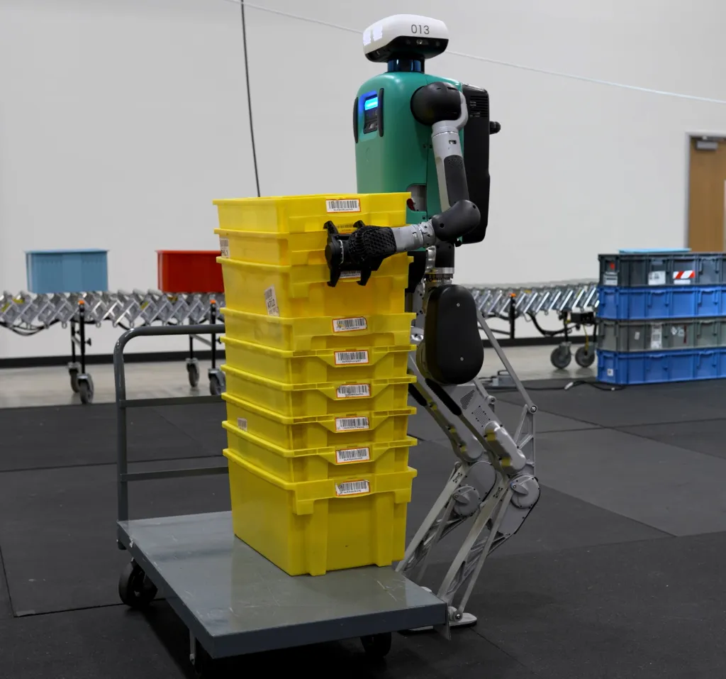 Agility Robotics Digit V4 robot pushing a cart loaded with yellow bins.