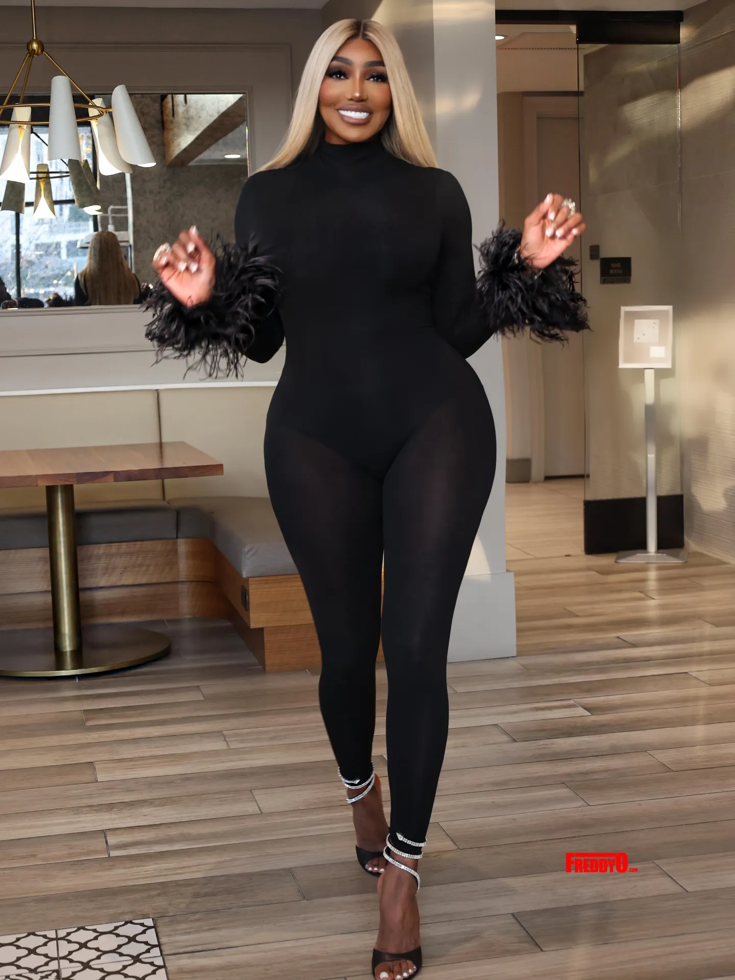 NeNe Leakes in a black jumpsuit with feathered sleeves and high heels.