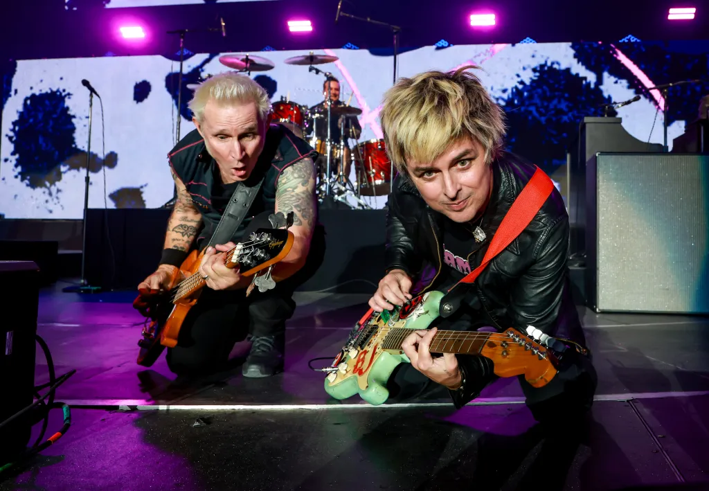 Mike Dirnt and Billie Joe Armstrong of Green Day crouch and play guitars on stage.