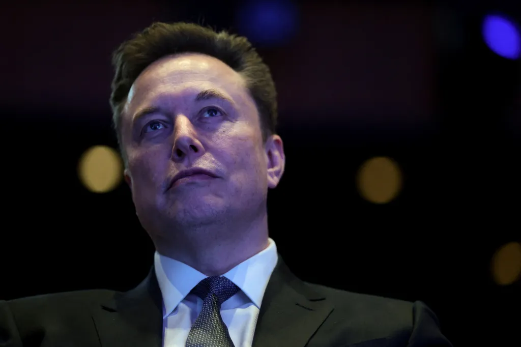 Close-up photo of Elon Musk looking up and slightly to the right, wearing a suit and tie.