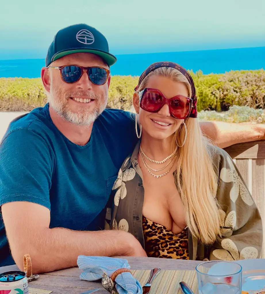 Jessica Simpson and Eric Johnson smiling at the camera outdoors, with the ocean in the background.