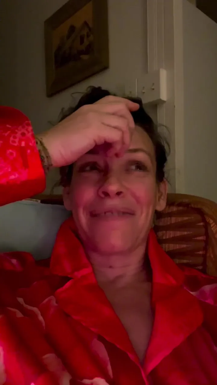 Evangeline Lilly in a red robe, clutching her forehead with a pained expression.