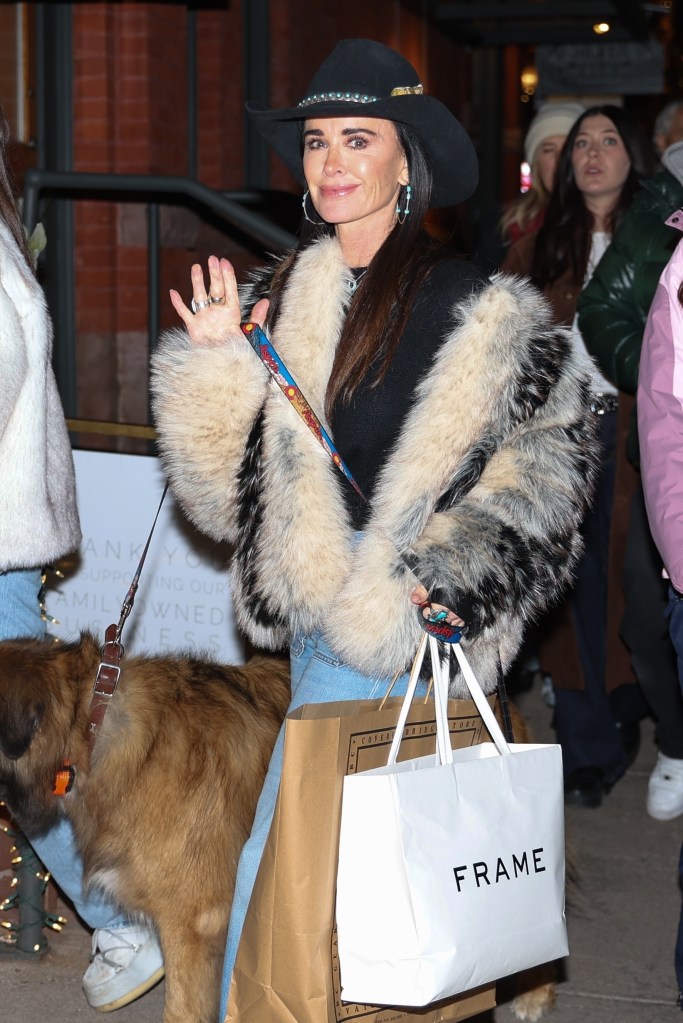 Kyle Richards in a fur coat and cowboy hat with her dog, holding a FRAME shopping bag.