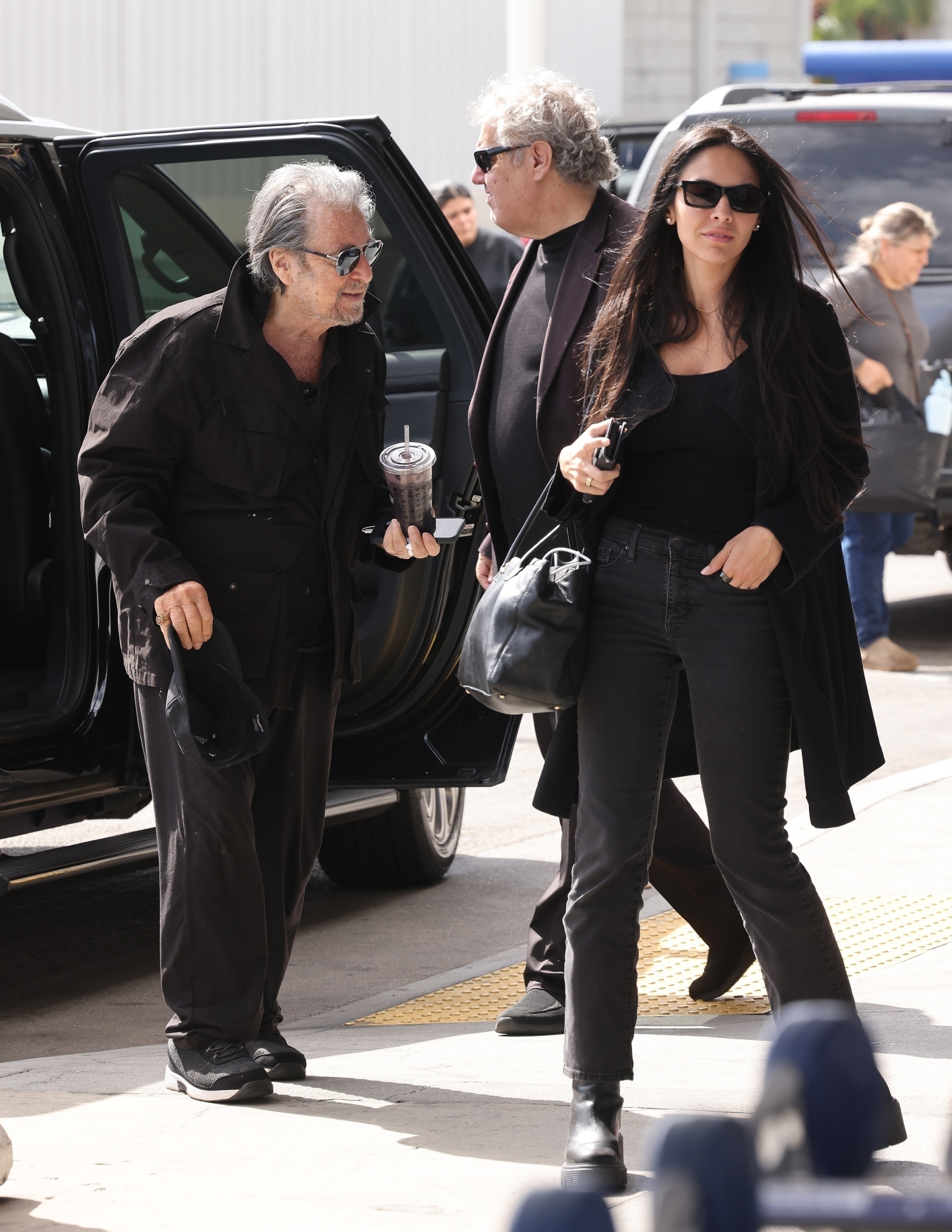 Al Pacino, with a drink in hand, and Noor Alfallah exiting a vehicle at LAX.