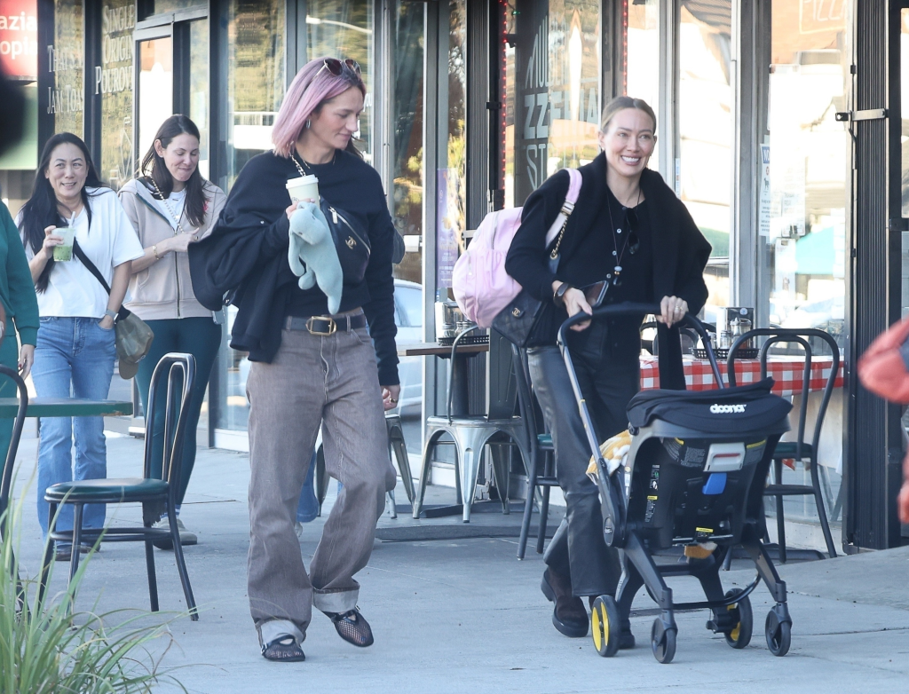 Hilary Duff smiling while pushing a baby stroller on a pizza outing with friends.
