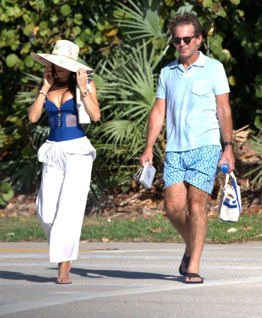 Bethenny Frankel, wearing a blue bustier, hat, and white slacks, walks next to a man in blue shorts and a polo shirt.