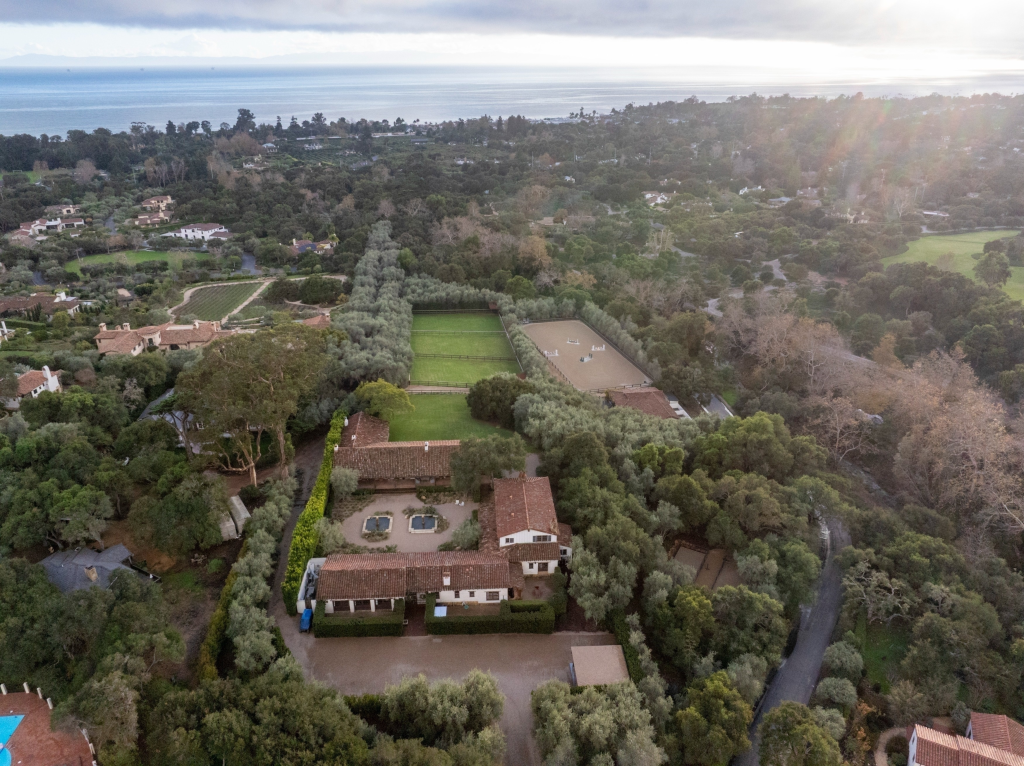 Aerial view of Kendall Jenner's Montecito estate with multiple buildings, lush trees, horse stables, and training facilities, with the ocean in the background.