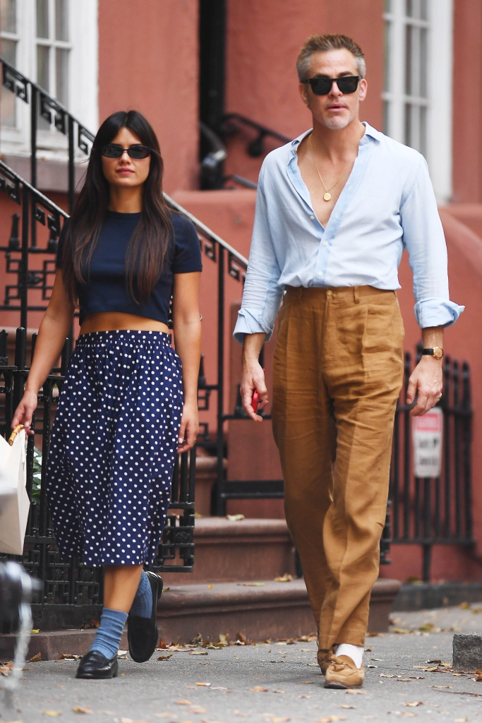 Chris Pine and Keana Sky Wenger walk outside in New York, with Keana wearing a blue crop top and polka dot skirt, and Chris wearing a light blue shirt and brown pants.