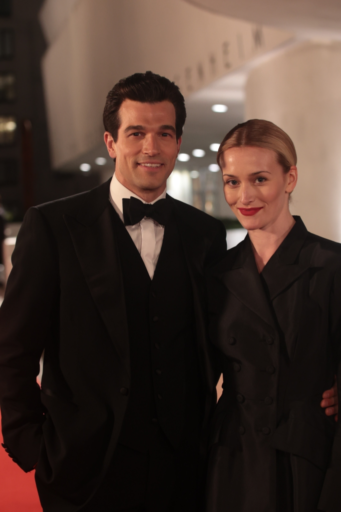 Paul Anthony Kelly and Sarah Pidgeon, dressed as JFK Jr. and Caroline Bissette, posing for a portrait at a black-tie event.