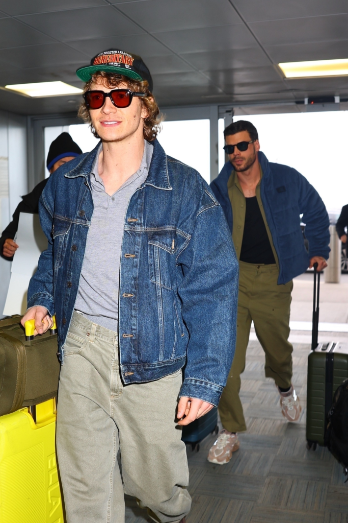 Connor Storrie and François Arnaud walking with their luggage in an airport terminal.