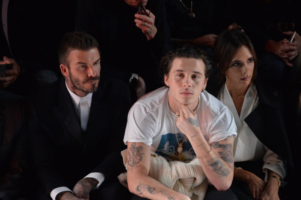 Brooklyn Peltz Beckham, David Beckham, and Victoria Beckham are seated, facing away from the camera.