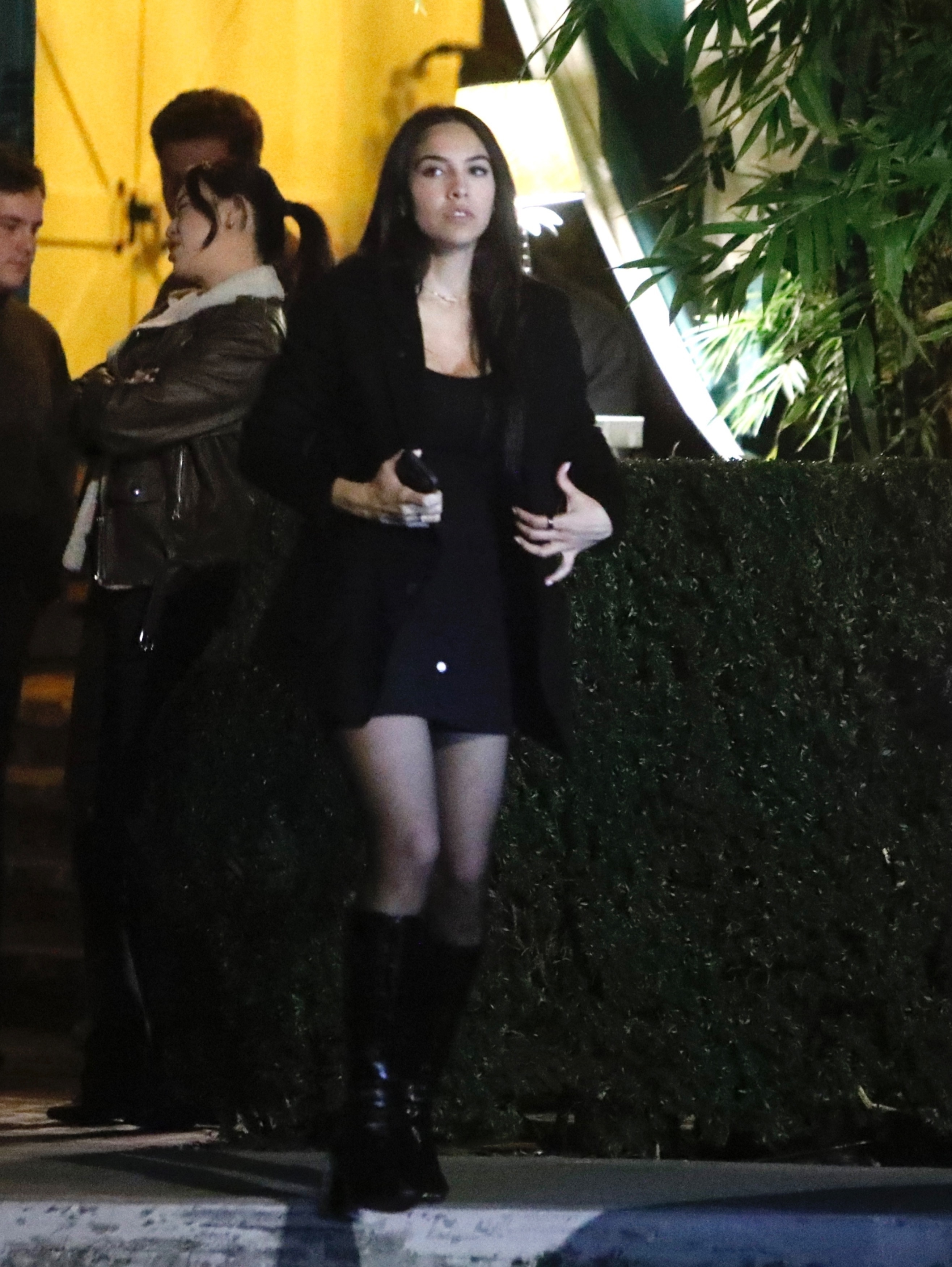 Noor Alfallah walking outside at night in a dark coat, mini skirt, and boots.
