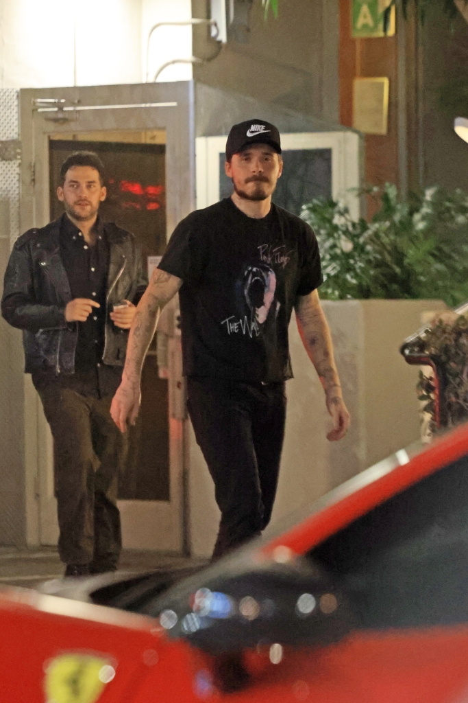Brooklyn Beckham in a black t-shirt and Nike hat, walking at night with a friend.