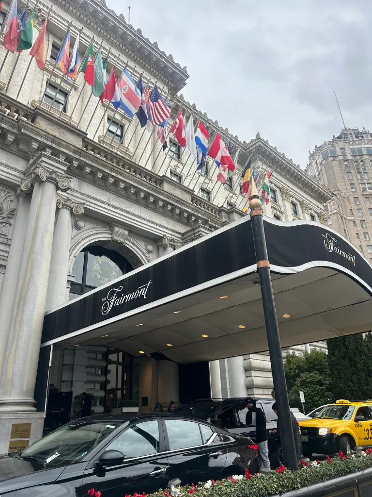 Fairmont Hotel in San Francisco, with an ornate building facade, a black awning over the entrance, and several flags flying.