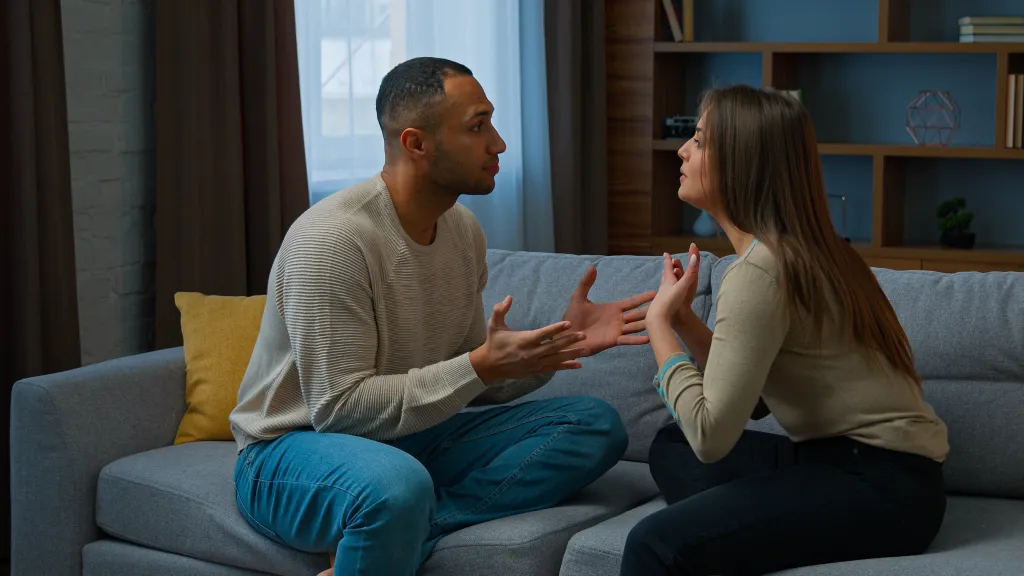 An African American man and Hispanic woman arguing on a gray couch.