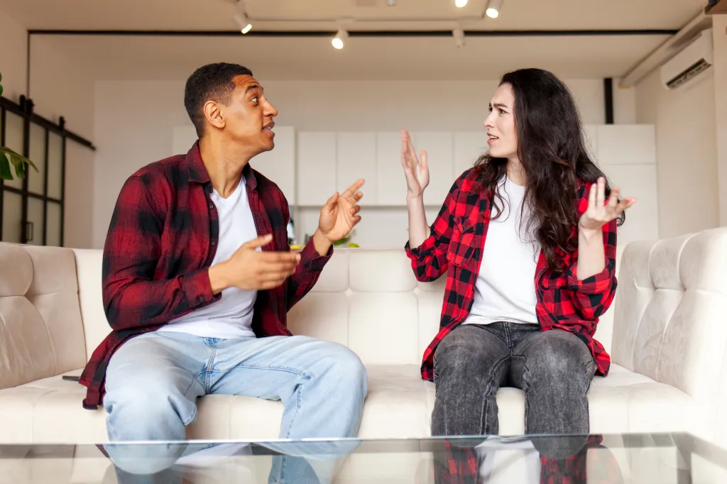 An interracial couple sitting on a couch, having a heated argument.