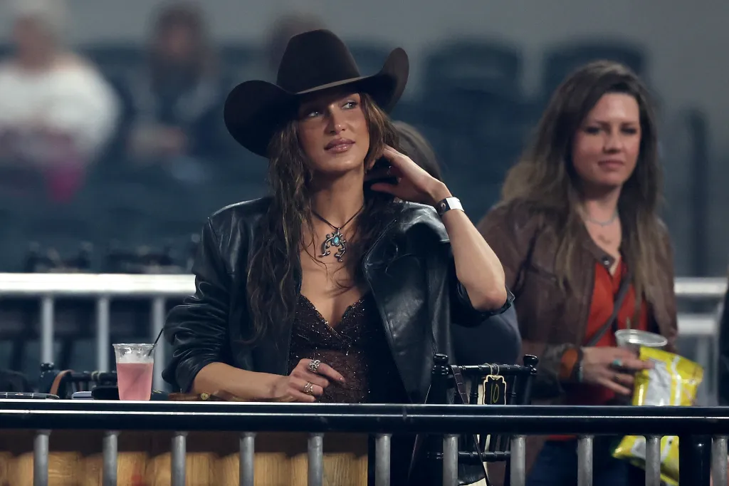 Fashion model Bella Hadid in a cowboy hat and black leather jacket looks on at an event.