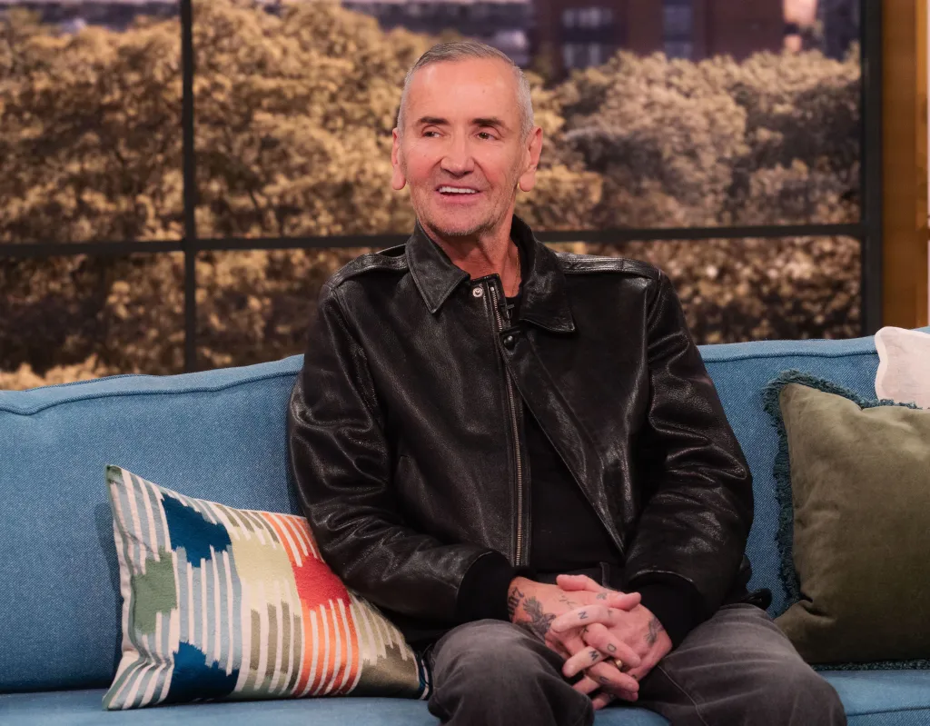 DJ Fat Tony, wearing a black leather jacket, sitting on a blue sofa.