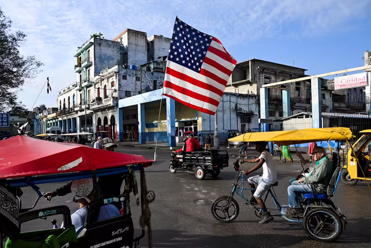 A large US flag is seen flying above street.