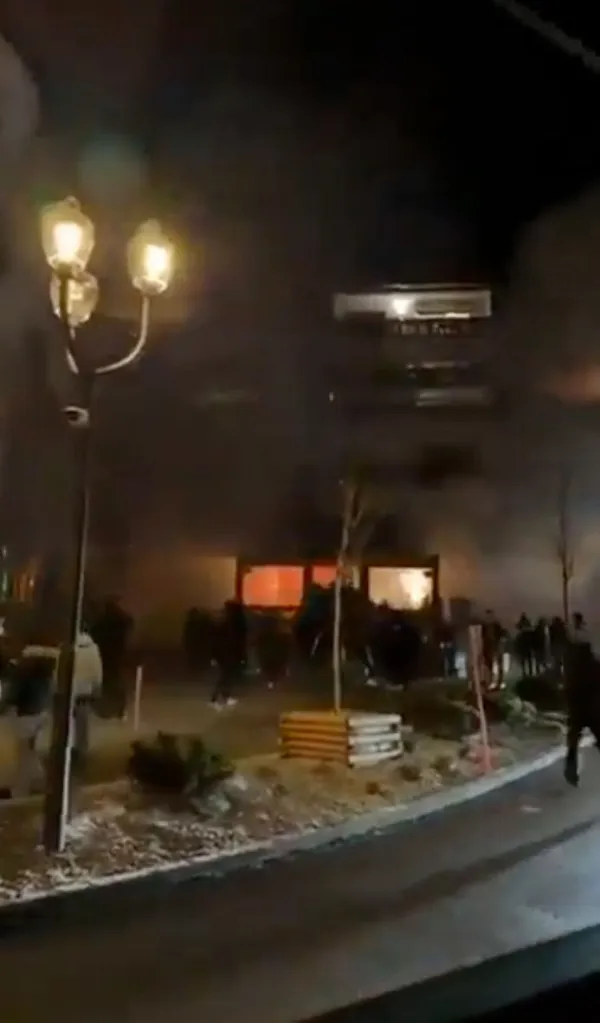 A building engulfed in flames and smoke with people standing nearby.