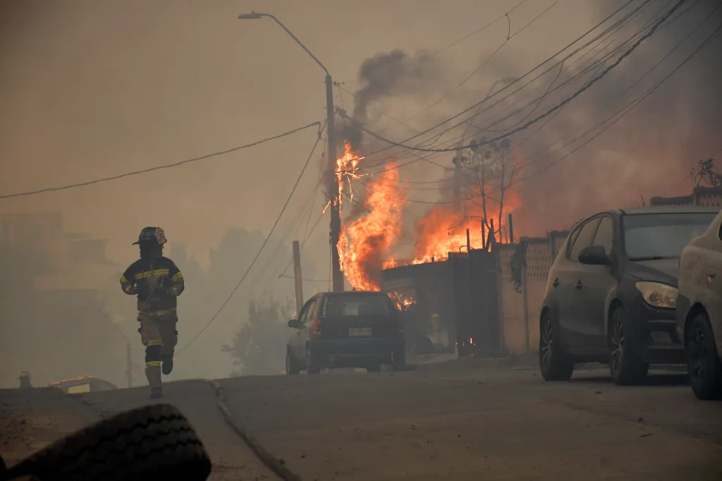 A firefighter runs along a street as a house burns during a wildfire in Concepcion, Chile, on January 18, 2026.