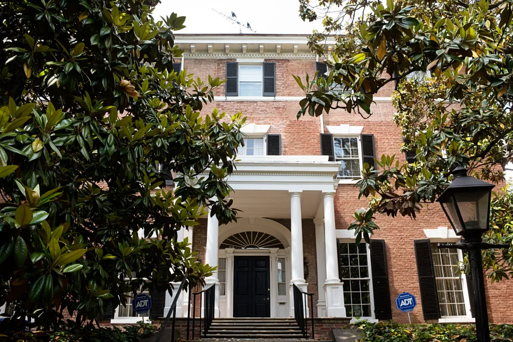 The brick facade of Jackie Kennedy's former home is framed by lush magnolia trees.