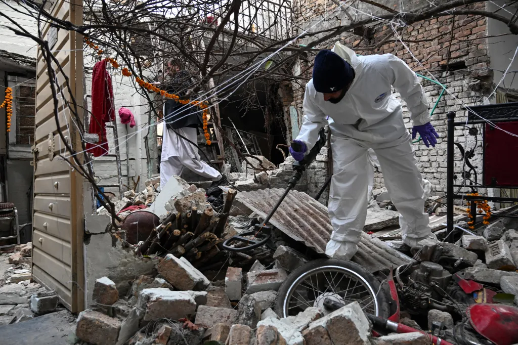 Forensic officials use metal detectors to inspect amid the debris of the damaged house