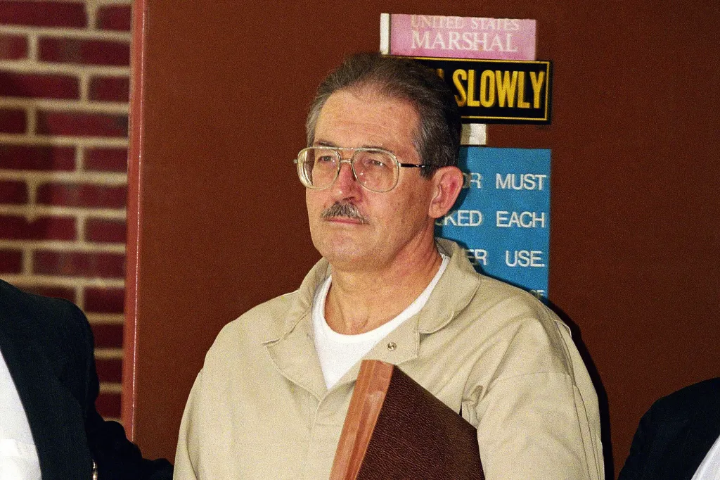 Aldrich Ames in a tan jumpsuit with a mustache and glasses.