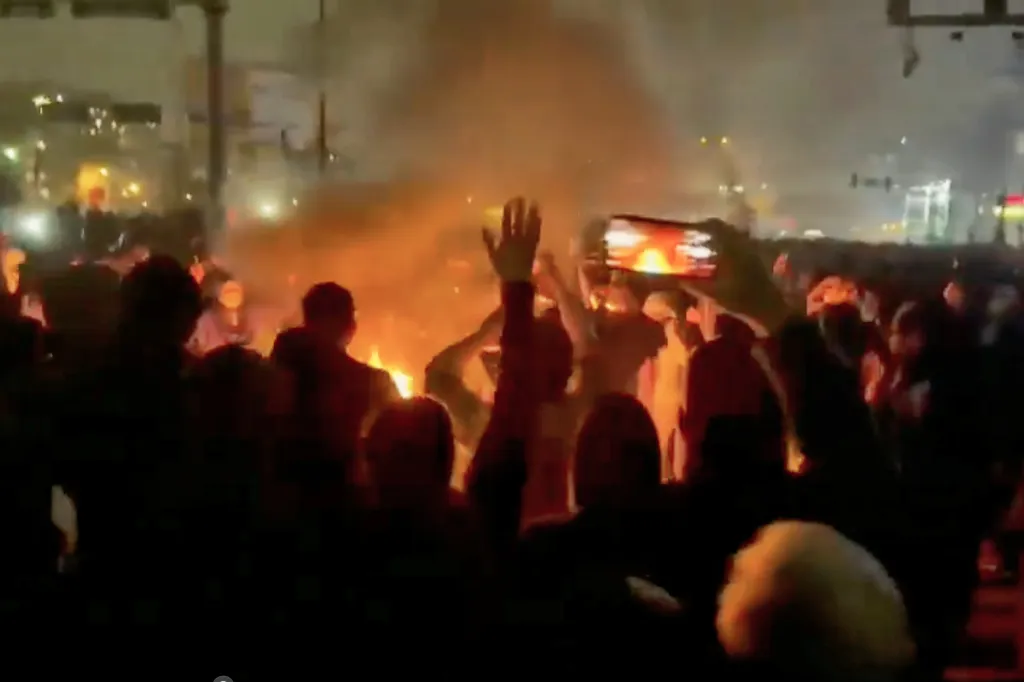 Protesters dancing around a bonfire in the street at night.