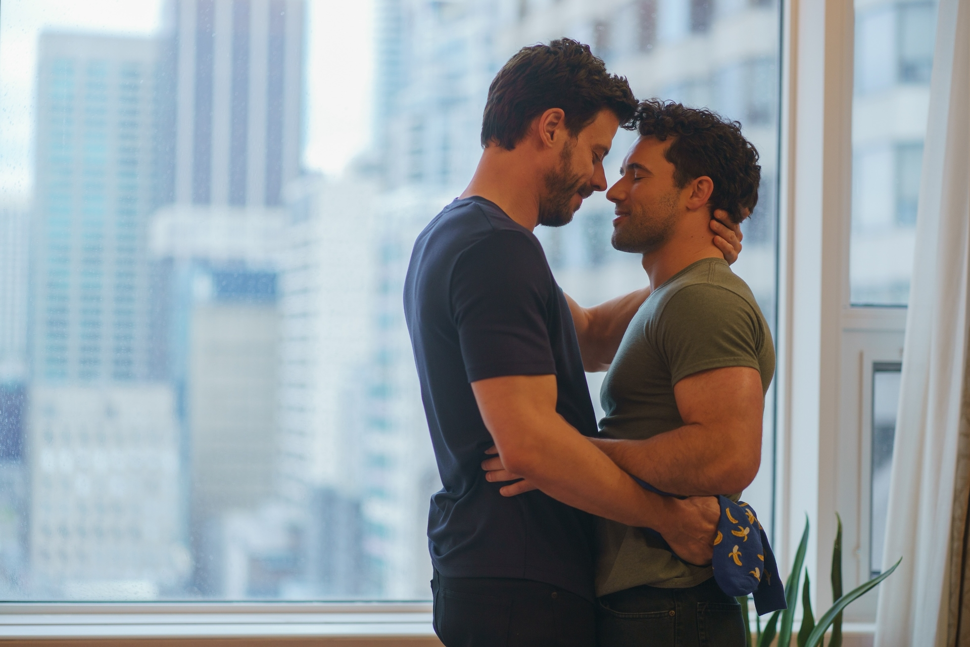 Scott Hunter and Kip Grady embraced in front of a city window.