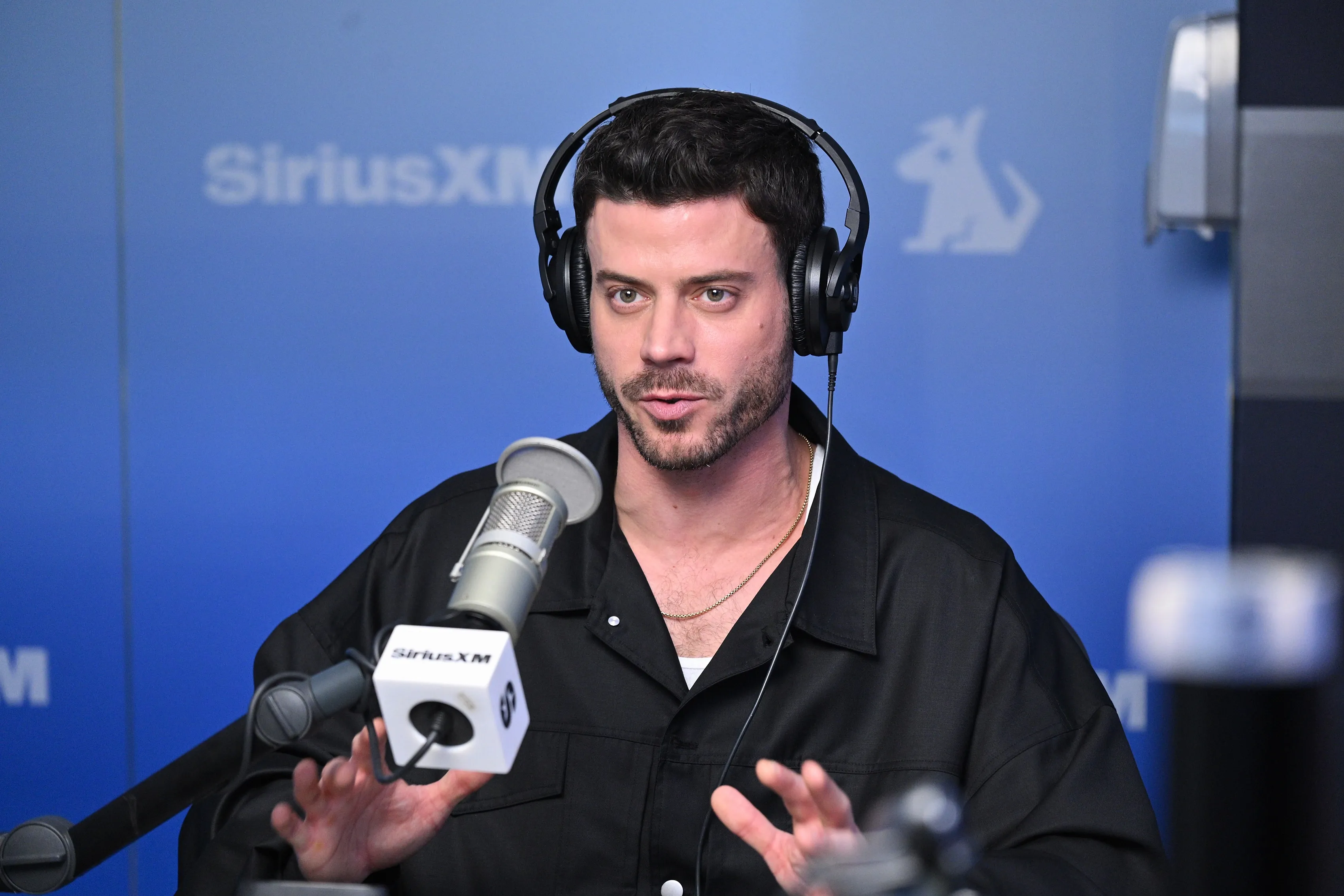 François Arnaud in a black shirt and headphones talking into a microphone at SiriusXM Studios.