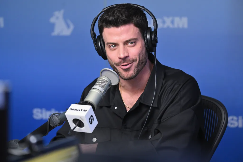 François Arnaud in headphones and a black shirt speaking into a SiriusXM microphone.