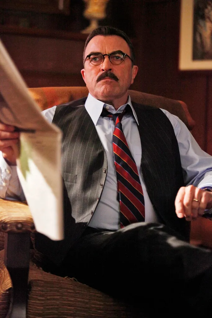 Frank Reagan (Tom Selleck) sitting in a chair holding a newspaper.