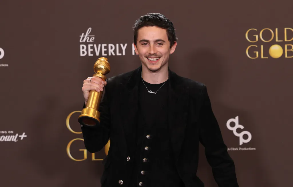 Timothée Chalamet smiling, holding a Golden Globe award.