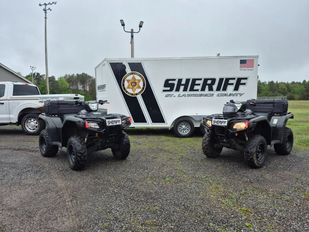 Two St. Lawrence County Sheriff's Office ATVs parked in front of a white trailer and a white pickup truck.